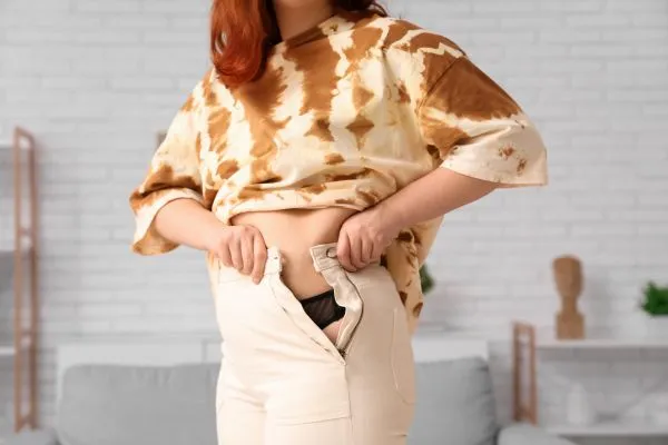 Image of woman trying to do her trousers up after pregnancy weight gain Liberton