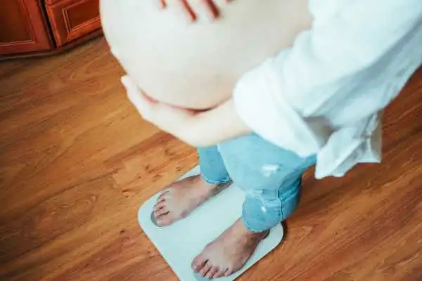 Image of woman weighing herself and experiencing weight gain through pregnancy Liberton